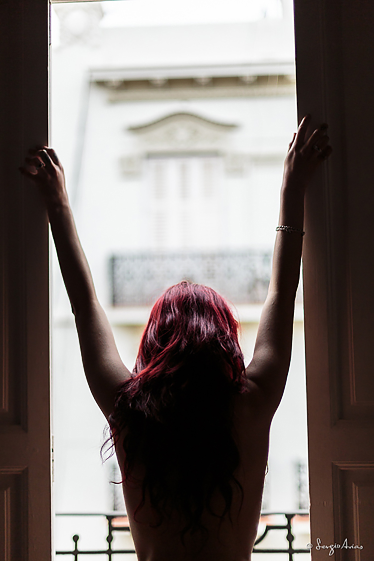 Chica de espaldas en una ventana con los brazos levantados
