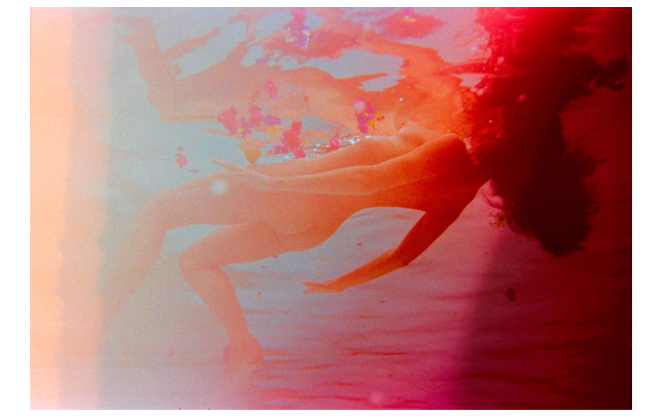 Chica flotando en la piscina en tonos rojizos